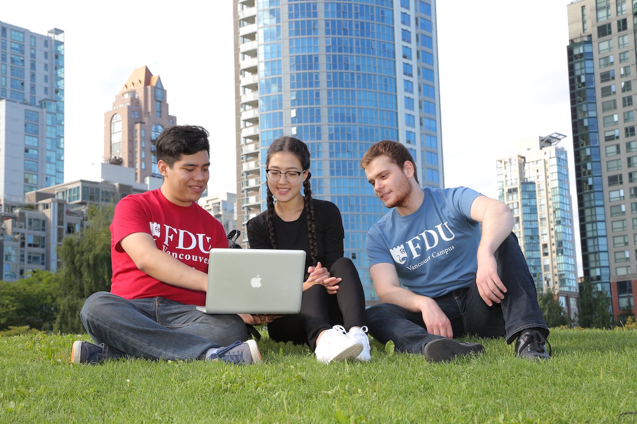 Three students sitting on the lawn looking at a laptop