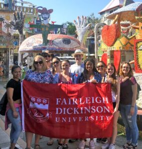 students smile for the camera. they hold up a flag that reads "Fairleigh Dickinson University."