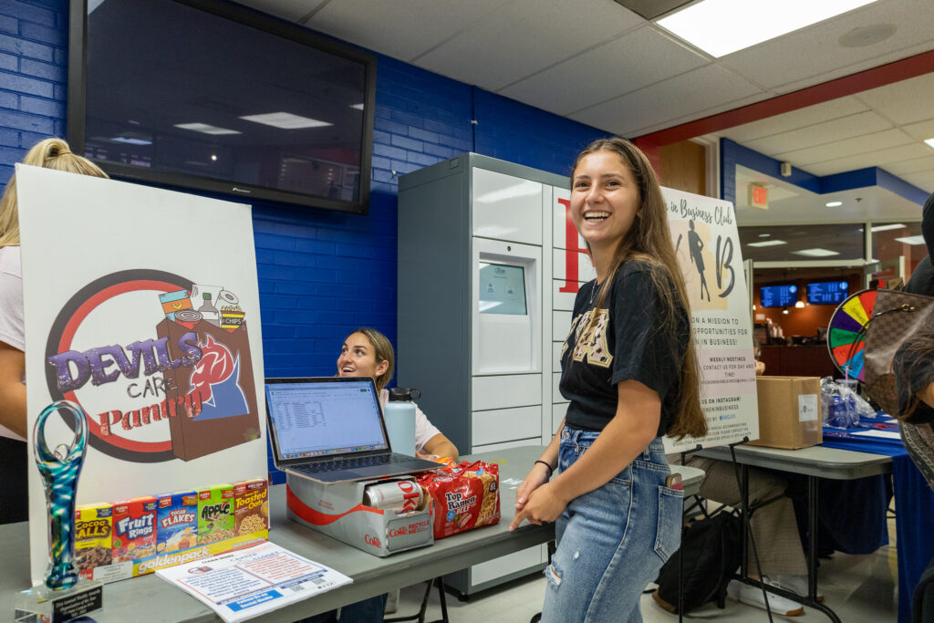 A student stands at a club's table at the club fair.