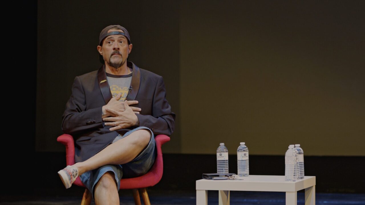 Kevin Smith sits in a chair on a stage