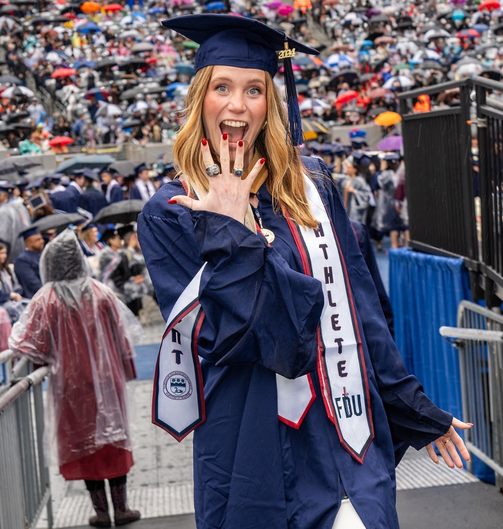 a graduate smiles at the camera and shows off her championship rings.