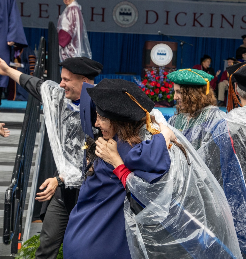 a graduate and a faculty member embrace in front of the commencement stage.