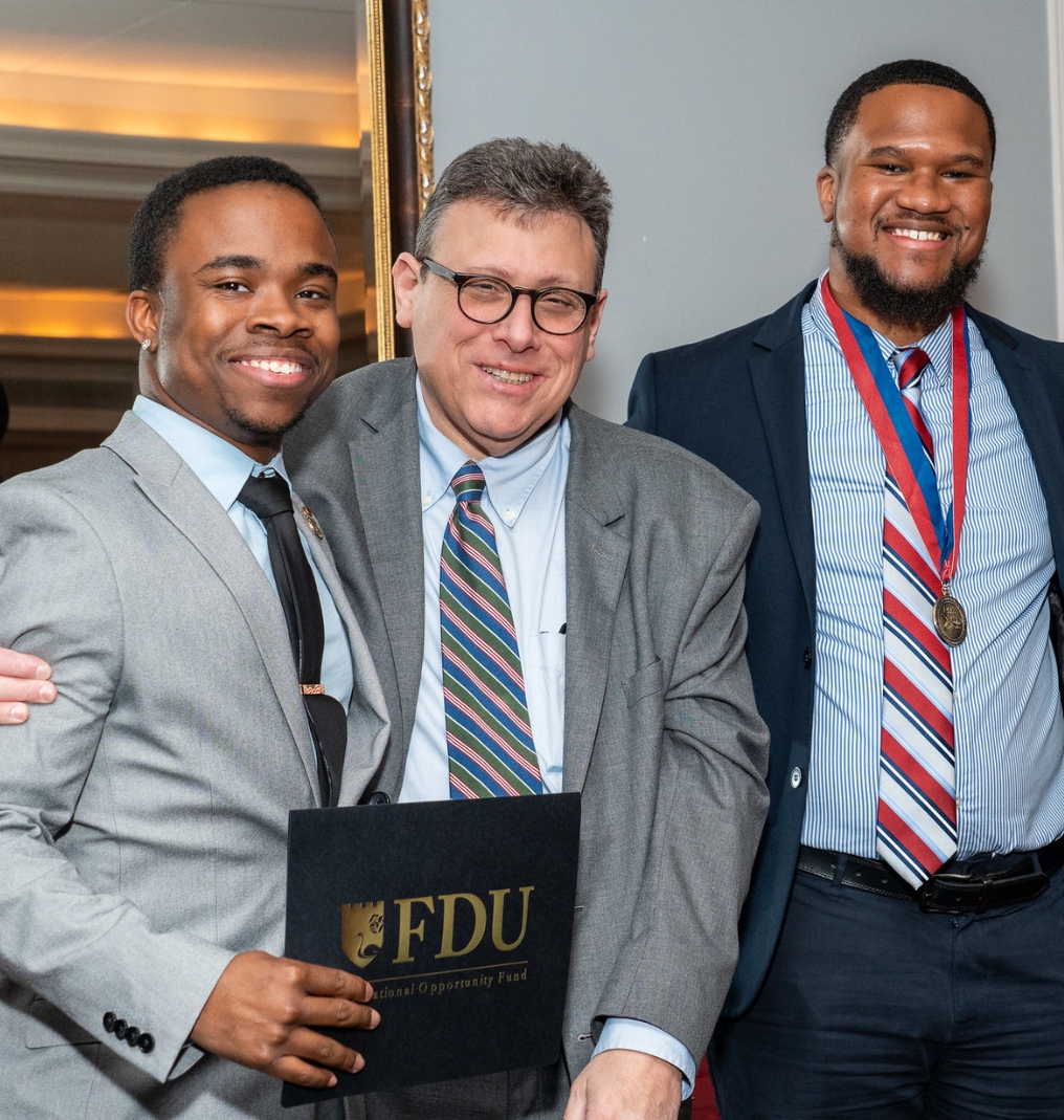 three men posing for the camera. they all smile and one holds an FDU Educational Opportunity Fund certificate.