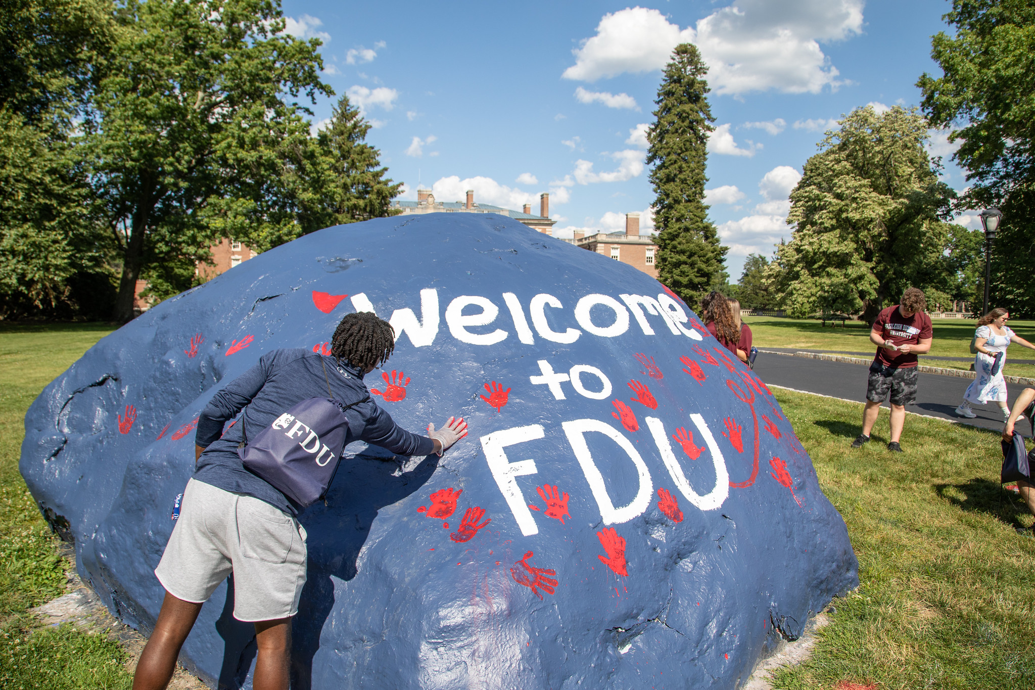 a student places a handprint on a large rock that reads "Welcome to FDU."