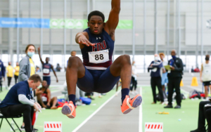 A young man competes in triple jump in track and field. He leaps into the air.