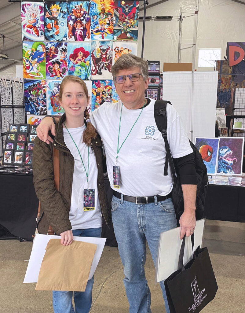 A middle-aged man puts his arm around his adult daughter. They are attending a comic festival.