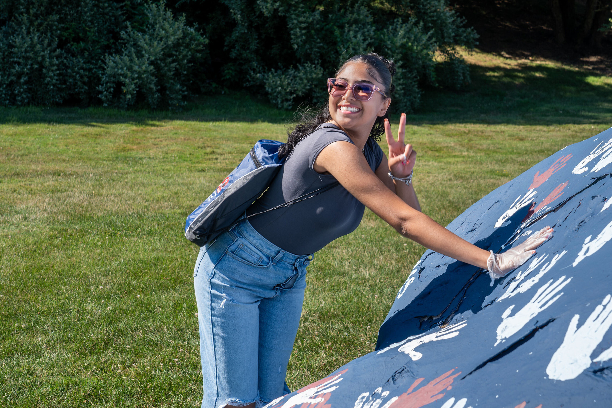 student places a handprint on a large rock. she throws a peace sign up to the camera.