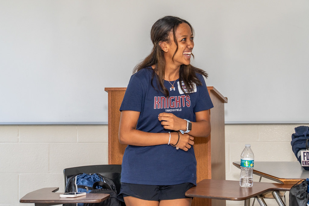 a student laughing and smiling at something out of frame. she wears an FDU knights track and field shirt.