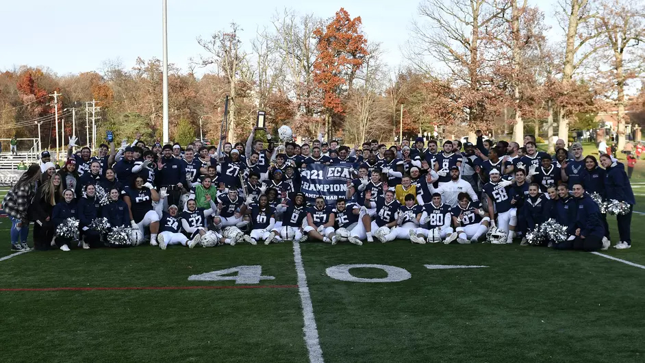 A football team in uniform poses on the football field with a winning banner. 