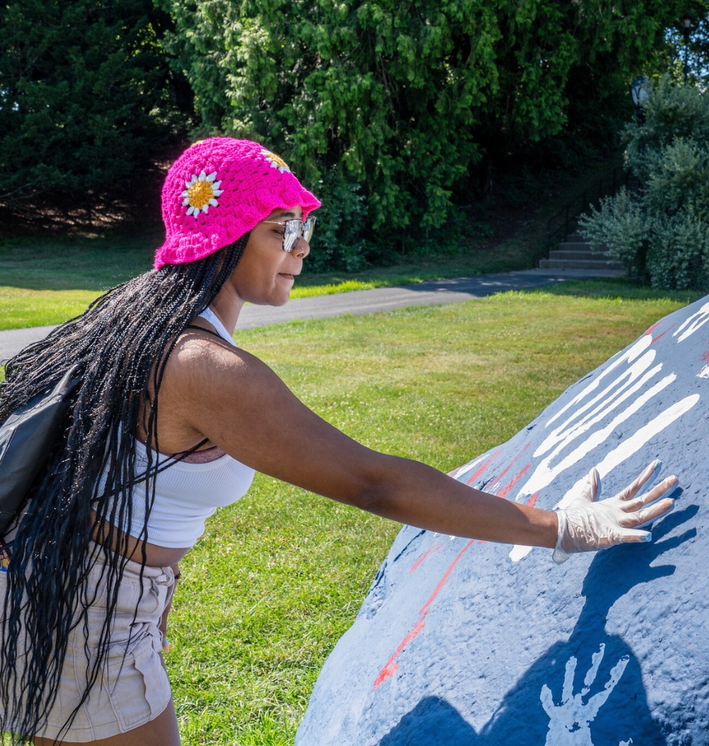 a student puts a handprint on a large rock.