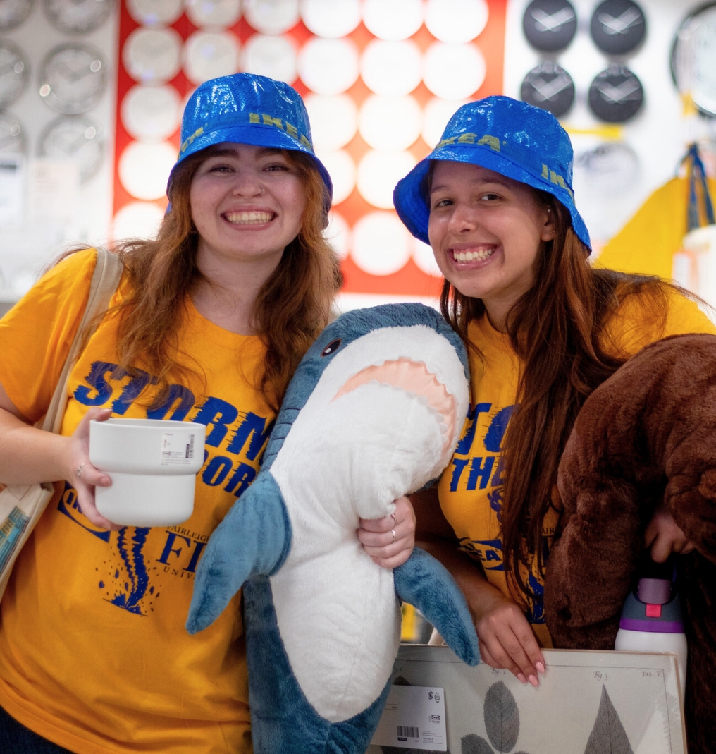 two students smile for the camera. they wear IKEA bucket hats and hold stuffed animals.