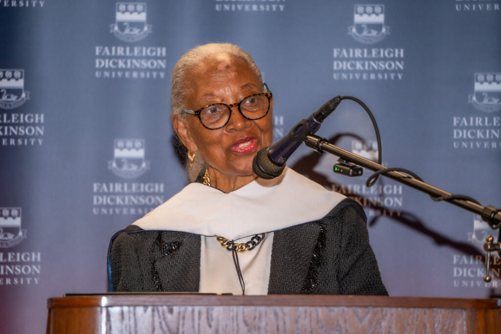 A woman wearing glasses speaks at a podium.