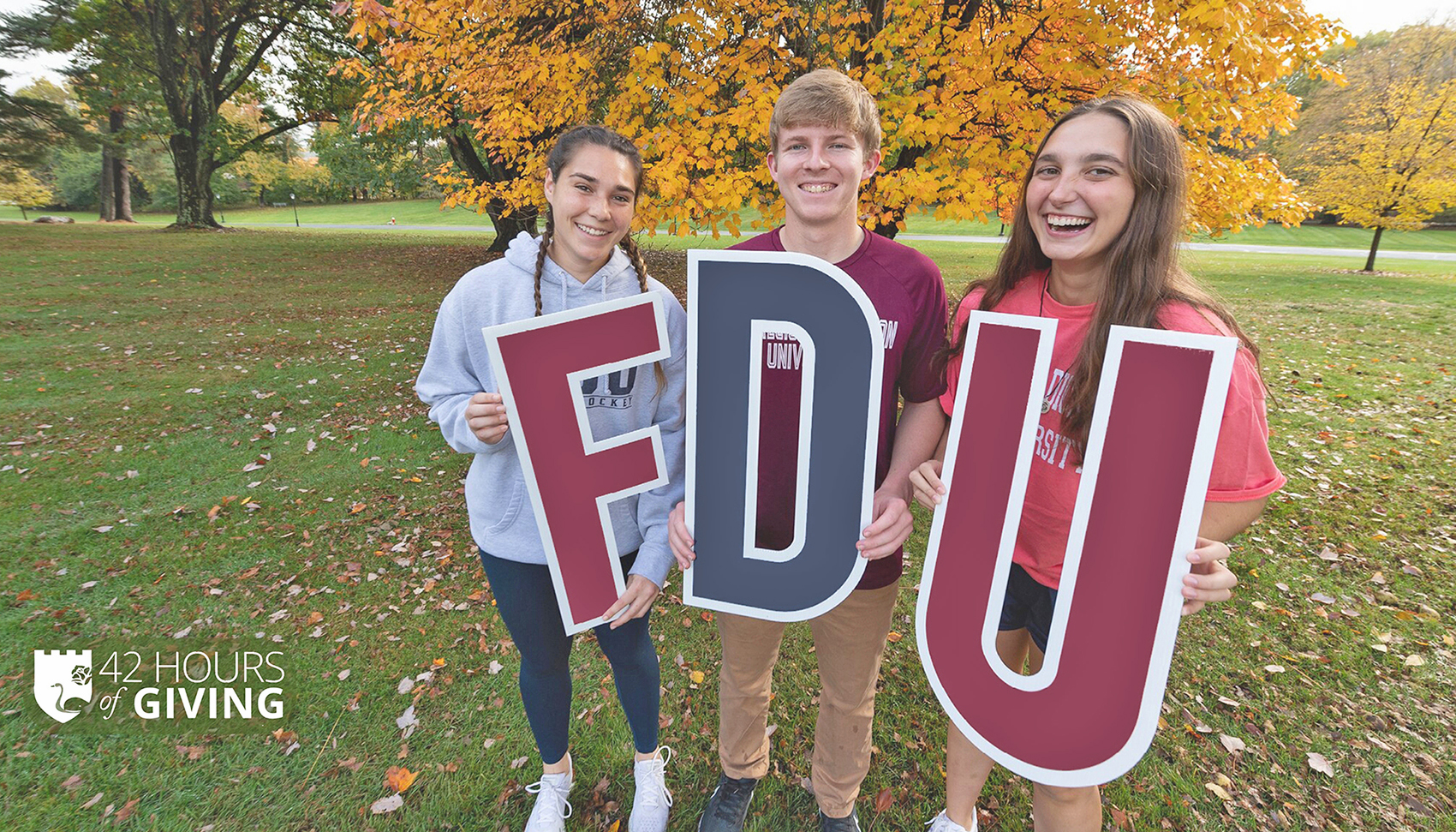 Three students hold up signs that spell out F-D-U.