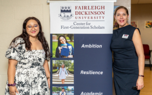 two women smile for the camera. they stand on either side of a roll-up banner. the banner reads "Fairleigh Dickinson University Center for First-Generation Scholars."