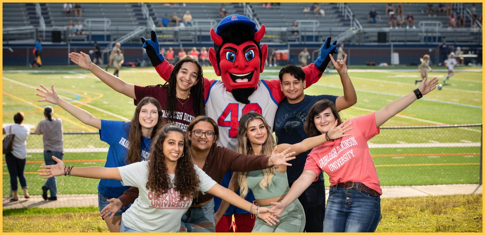 students and the Ian the Devil mascot smile for the camera. they hold on their arms.