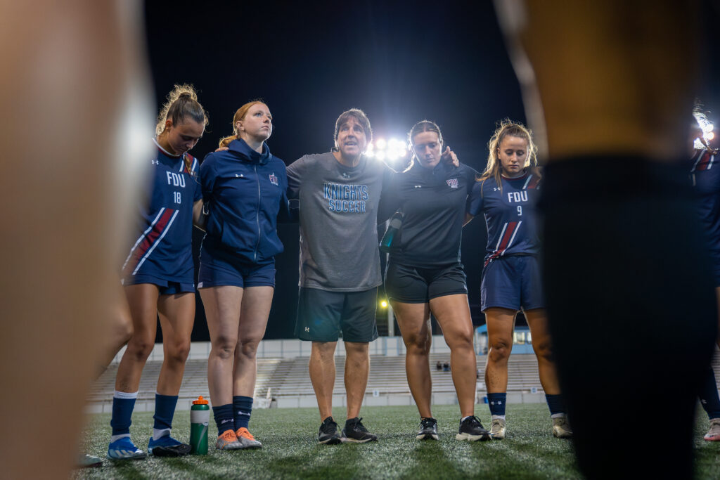 A group stands arm in arm before a soccer match at night.