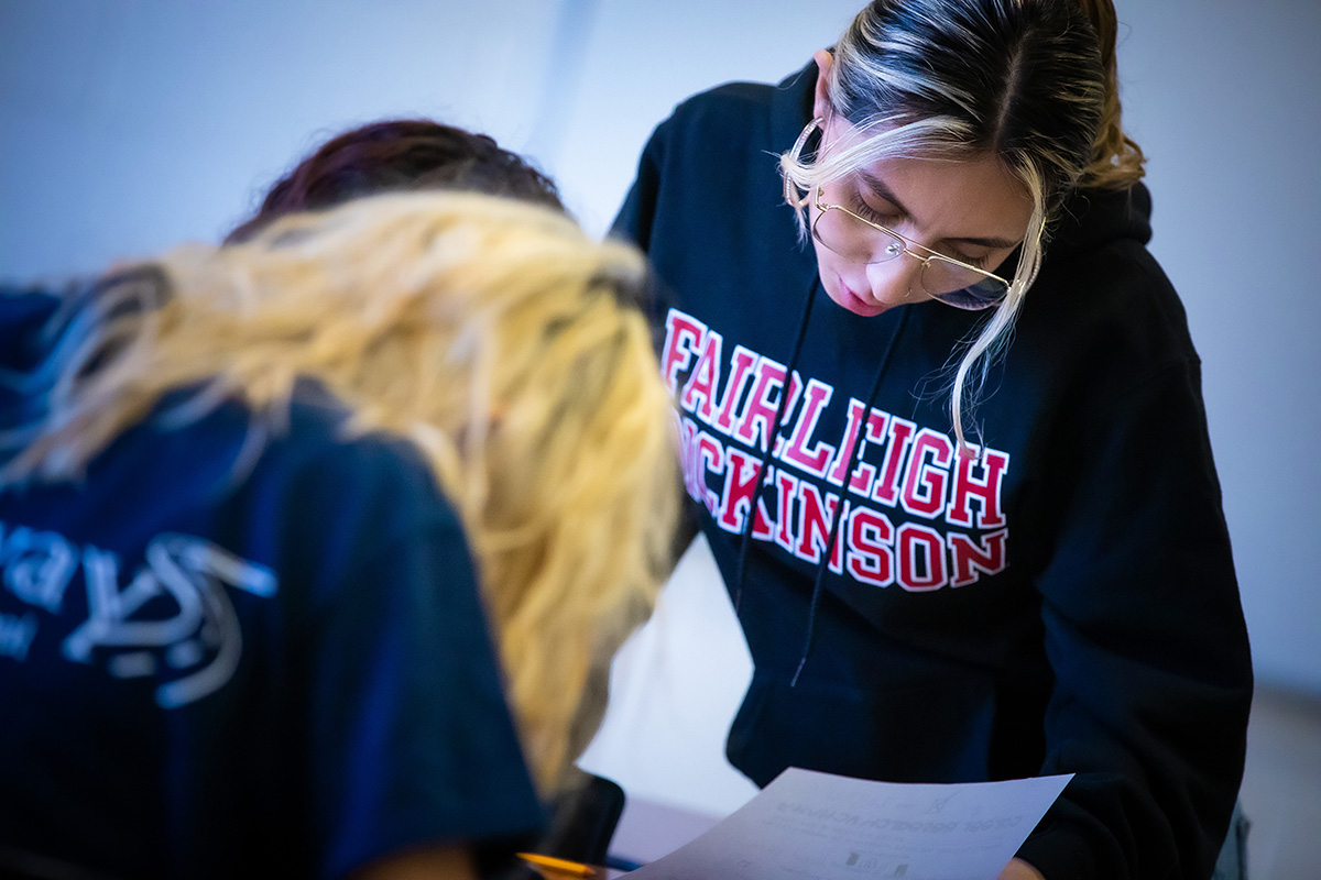 A young woman leans over to help a middle school student.