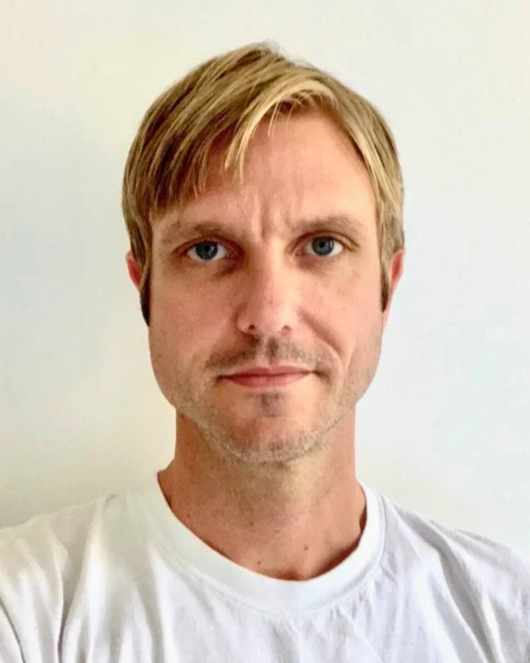 portrait of a man against a wall. he wears a white shirt.