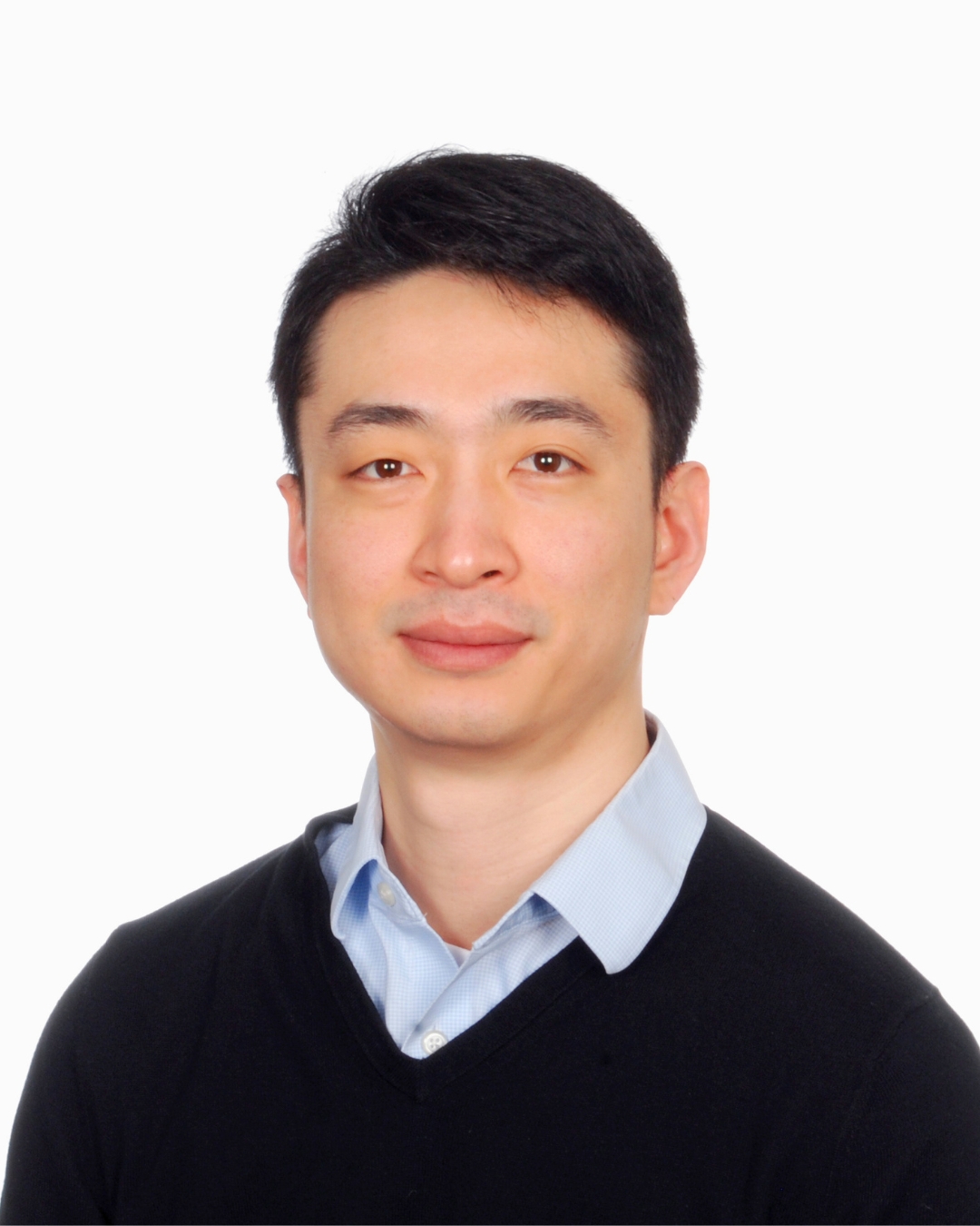 portrait of a man against a white background. he wears a black sweater and collared shirt underneath.