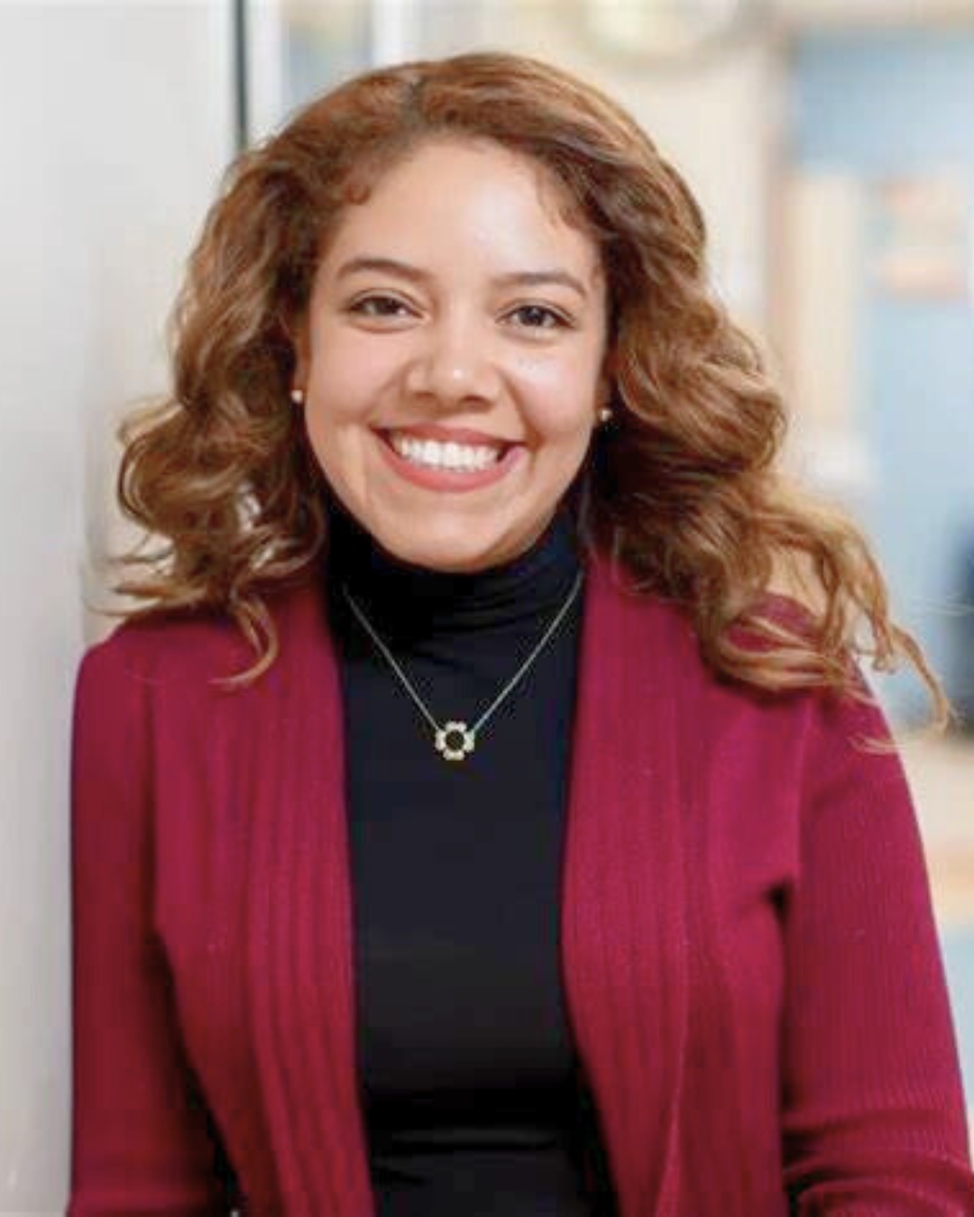 portrait of a woman leaning against a wall. she wears a red cardigan.