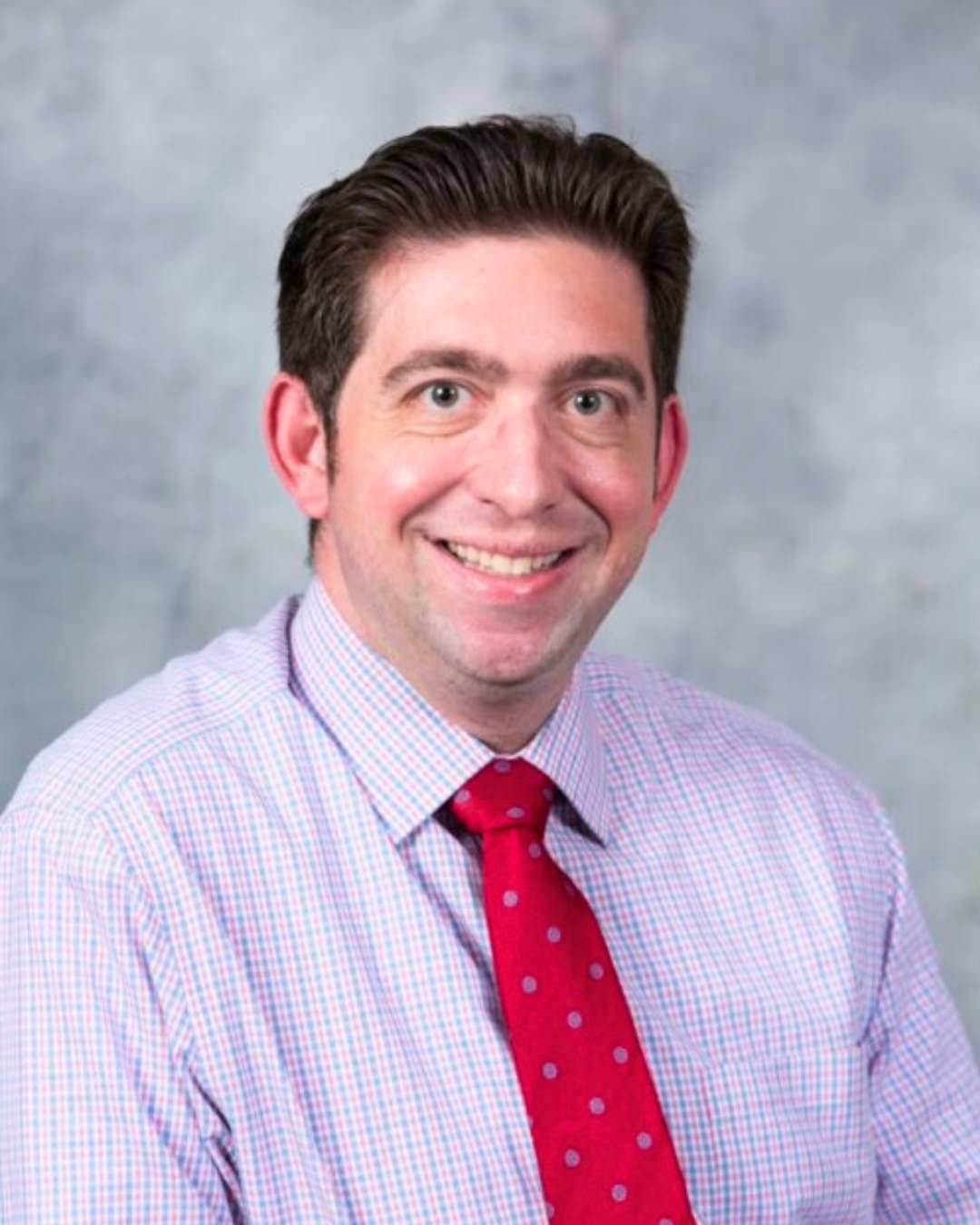 portrait of a man against a gray backdrop. he wears a red tie.