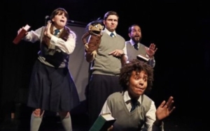 actors on a stage. they wear school uniforms and one holds a puppet.