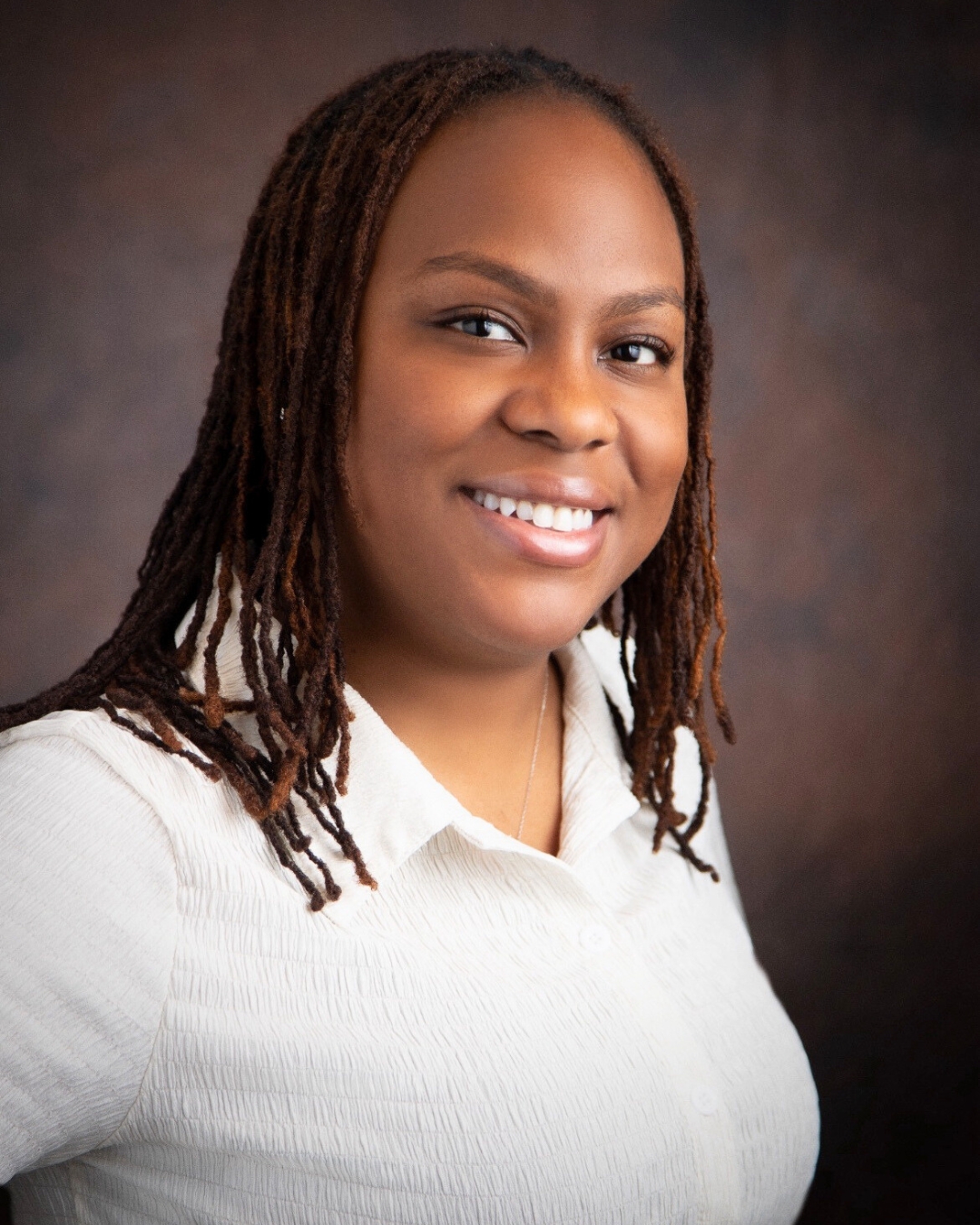 portrait of a woman against a brown backdrop. she wears a white shirt.