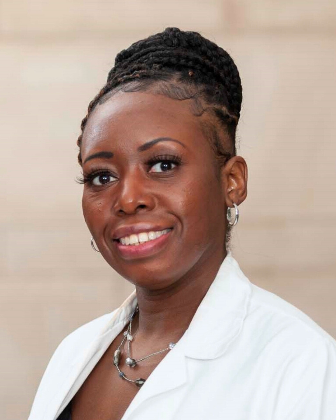 portrait of a woman against a wall. she wears a white lab coat.