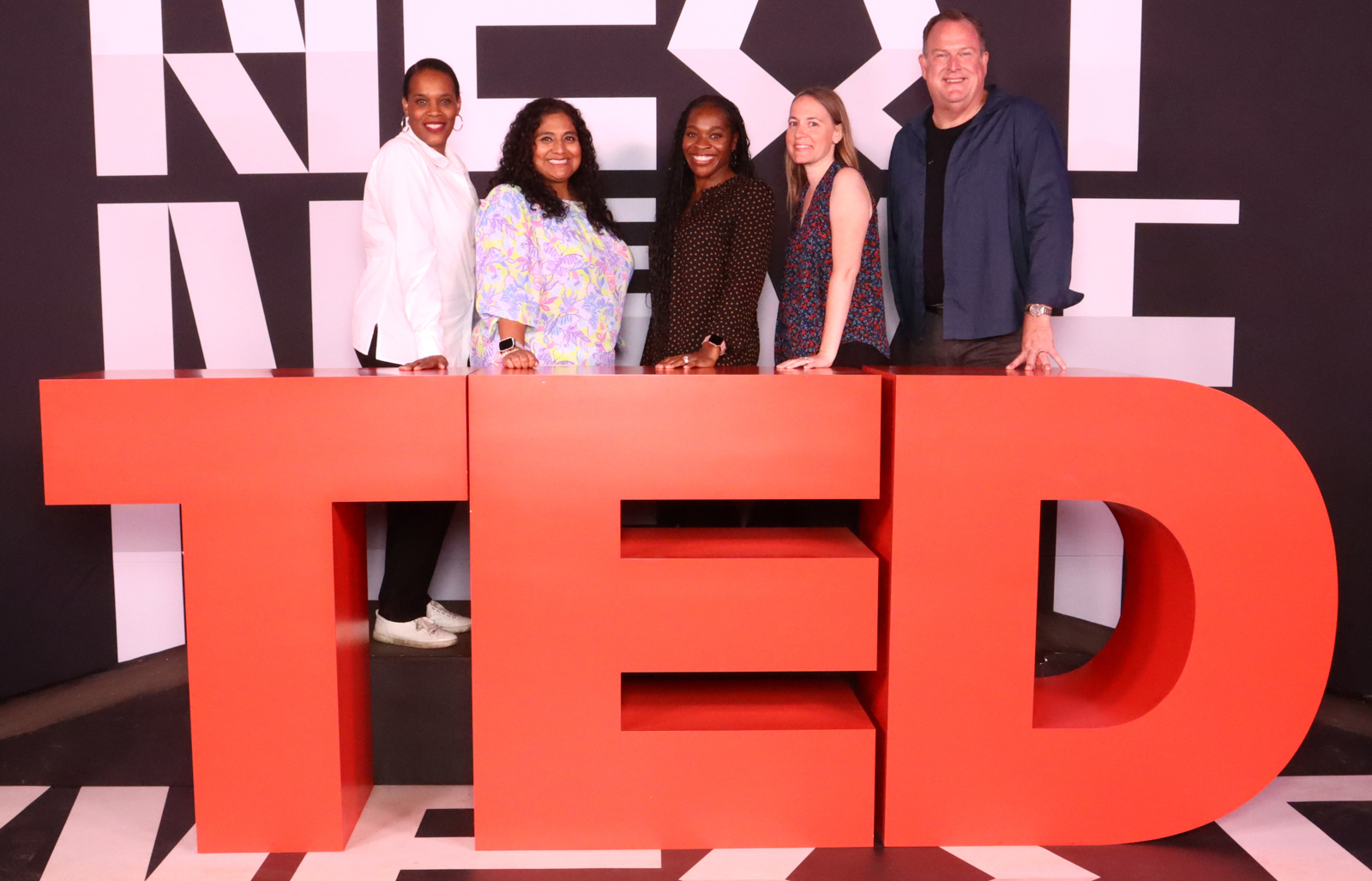 a group of people smile and pose for the camera. they stand behind large block TED letters.