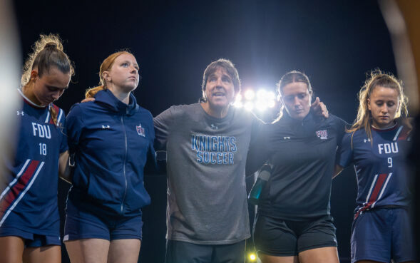 A group stands arm in arm before a soccer match at night.