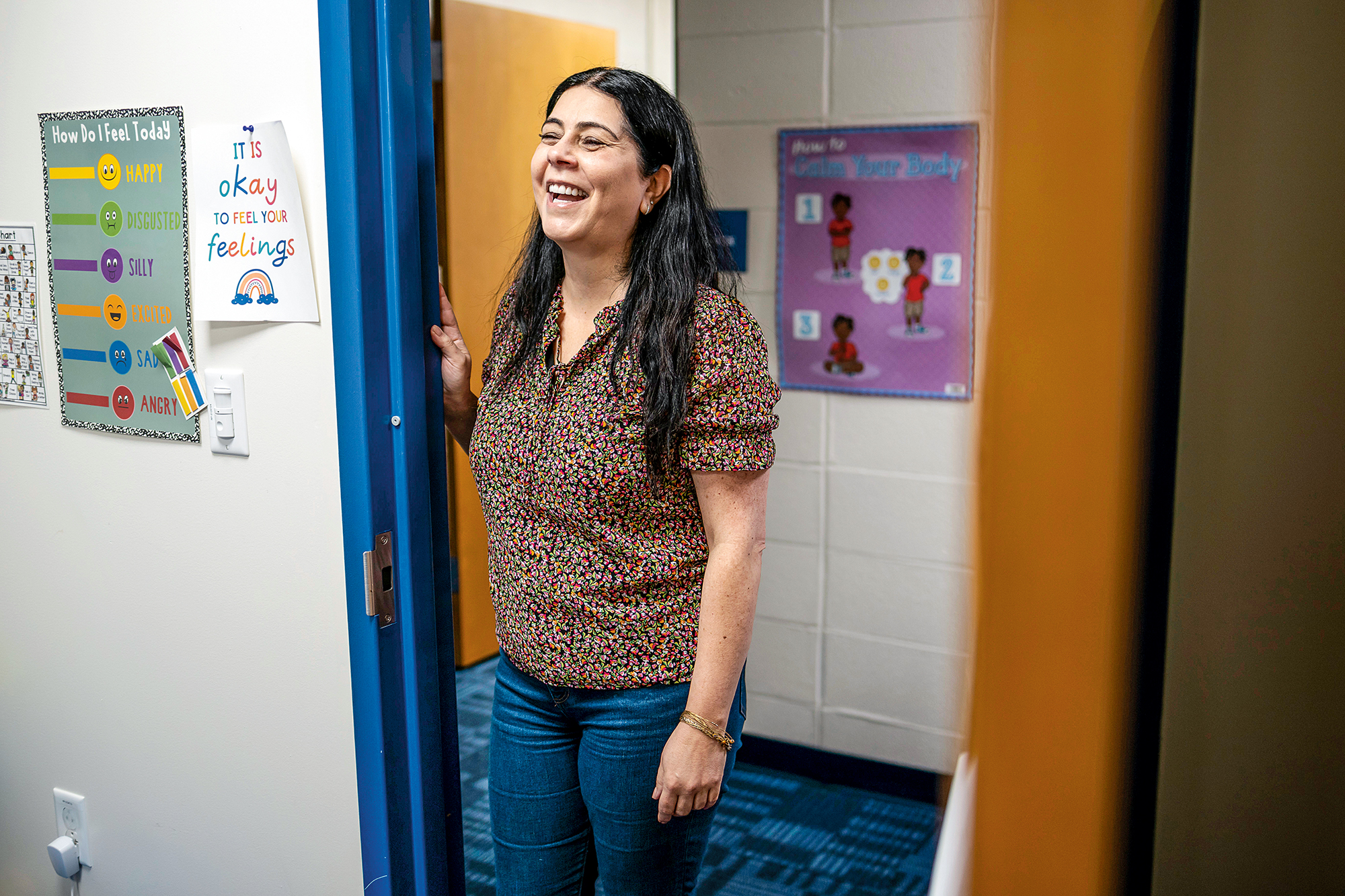 A woman stands in the doorway of an elementary school hallway.