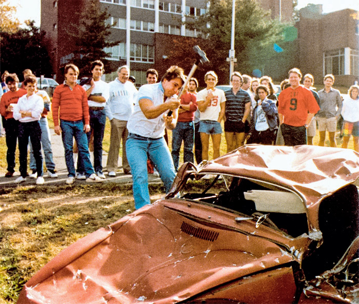 A young man raises a sledgehammer to smash a car at a traditional car smash event.