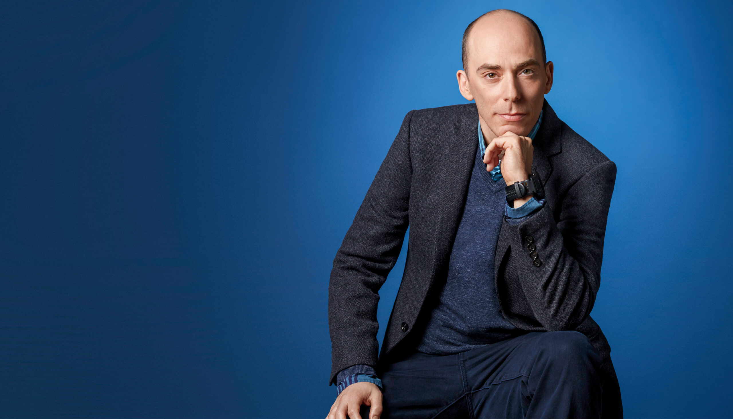 Portrait of a man against a blue photo backdrop.