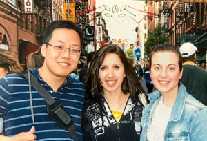 Three college students, one man and two women, pose for an outdoor photo at a festival in New York City.