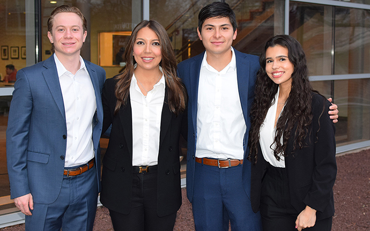 Four students stand in a line, posing for a photo. Two are male, two are female.