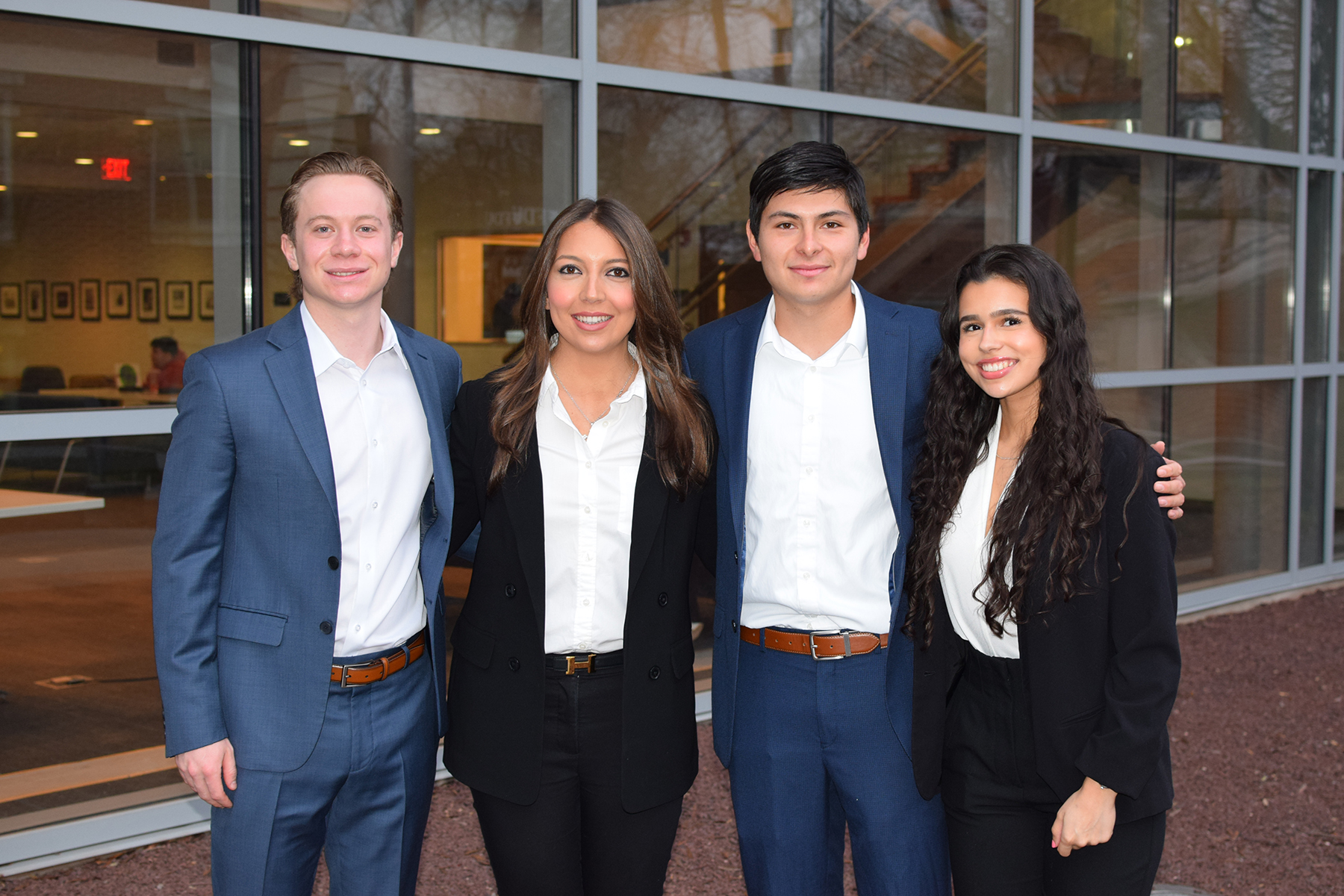 Four students stand in a line, posing for a photo. Two are male, two are female.